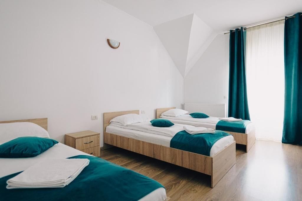 A modern hotel room with two single beds, wooden headboards, and teal bedding.