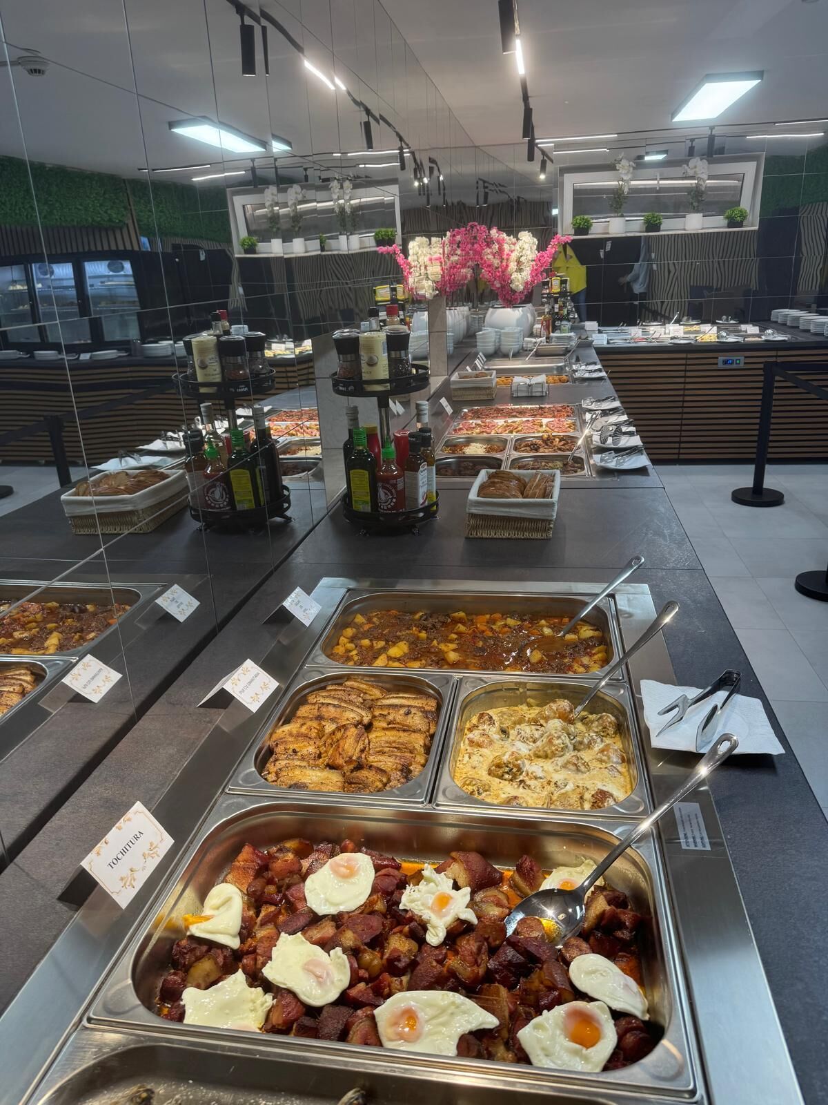A buffet with various food options, condiment dispensers, and a decorative floral arrangement.