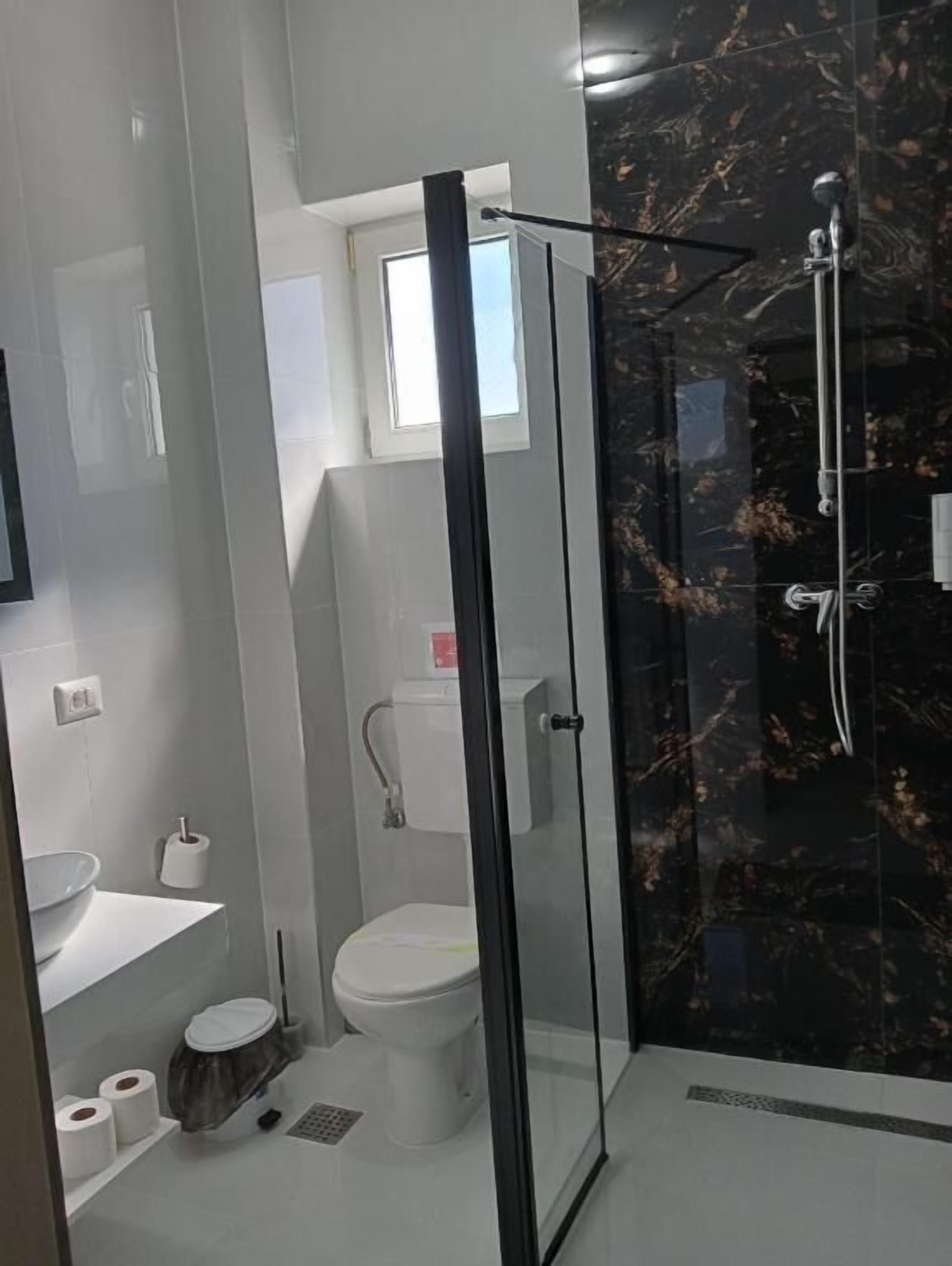 A modern bathroom with a glass-enclosed shower, a toilet, a sink, and a toilet paper holder.