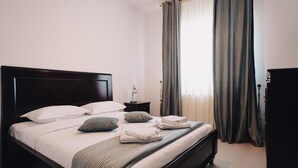 A neatly made bed with pillows and folded towels, a bedside table with a lamp, and a dark wooden headboard.