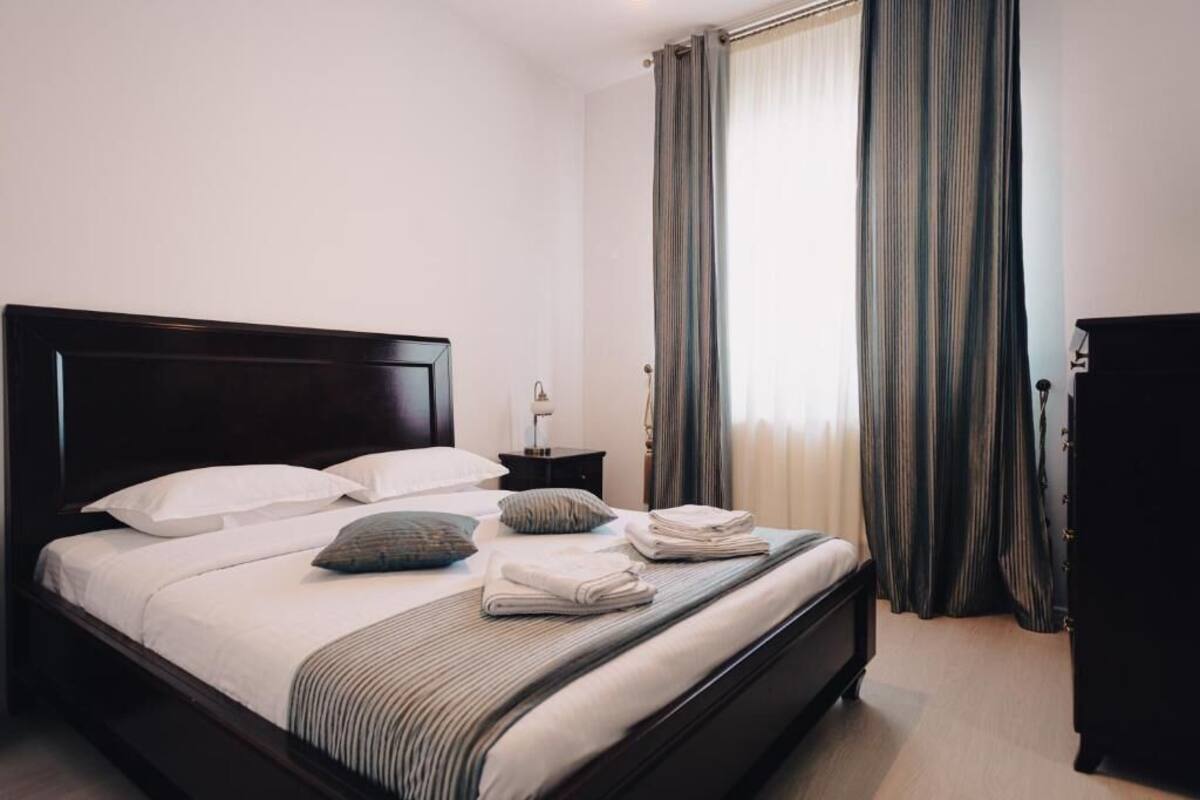 Una cama bien hecha con almohadas y toallas dobladas, una mesita de noche con lámpara y un cabecero de madera oscura.