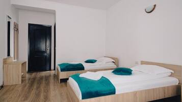 Una habitación con dos camas de madera, cada una con ropa de cama y almohadas color turquesa, un escritorio de madera y una puerta negra.