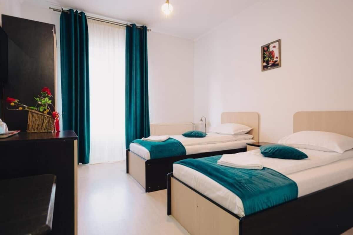 Habitación de hotel con dos camas individuales, un escritorio, una silla y una ventana con cortinas.