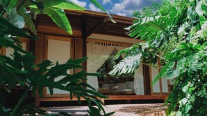 Une maison traditionnelle en bois, dotée de grandes fenêtres en verre et entourée d’une végétation luxuriante.