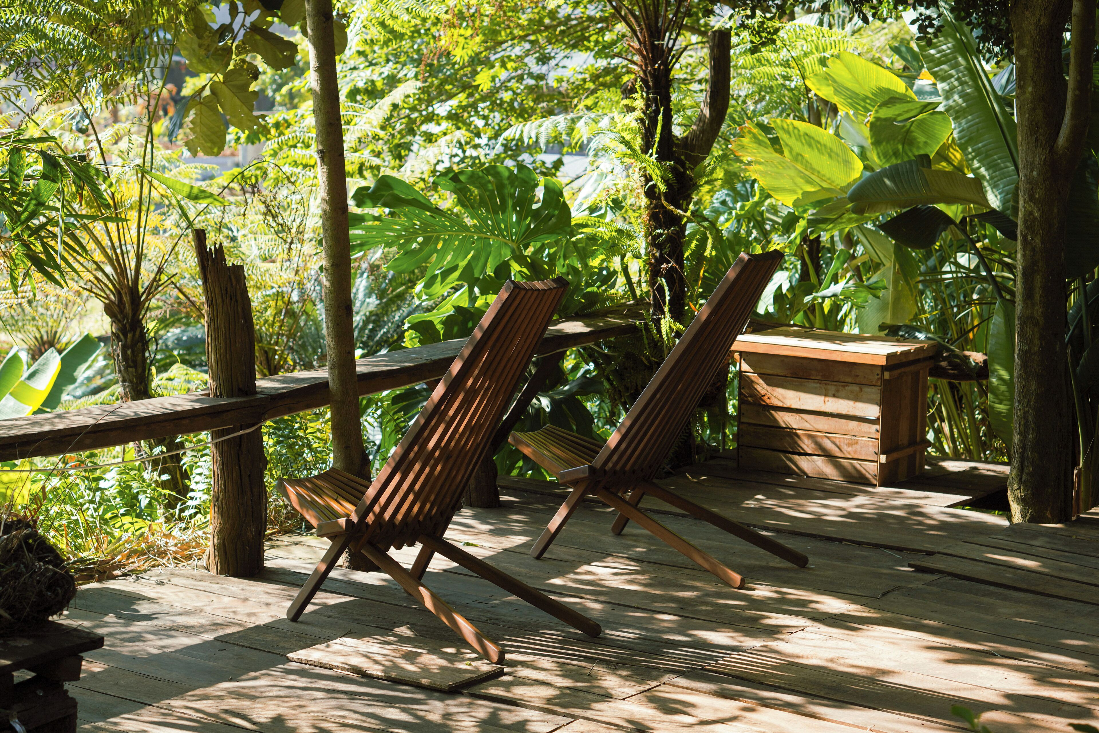 Dues cadires de relax de fusta sobre un pont de fusta envoltat de vegetació tropical exuberant.