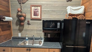 Una cucina con mobili in legno, un lavello in acciaio inossidabile, un forno a microonde e un frigorifero nero.