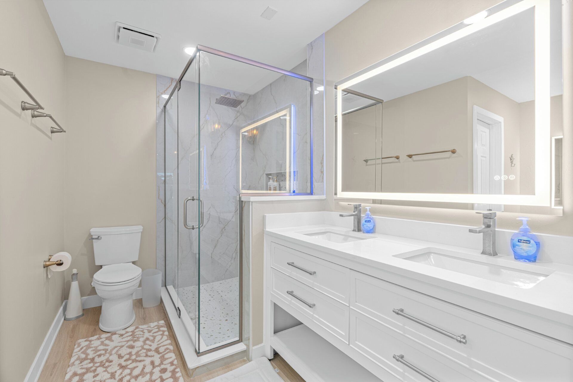 A modern bathroom with a glass-enclosed shower, a white vanity with a large mirror, and a toilet.