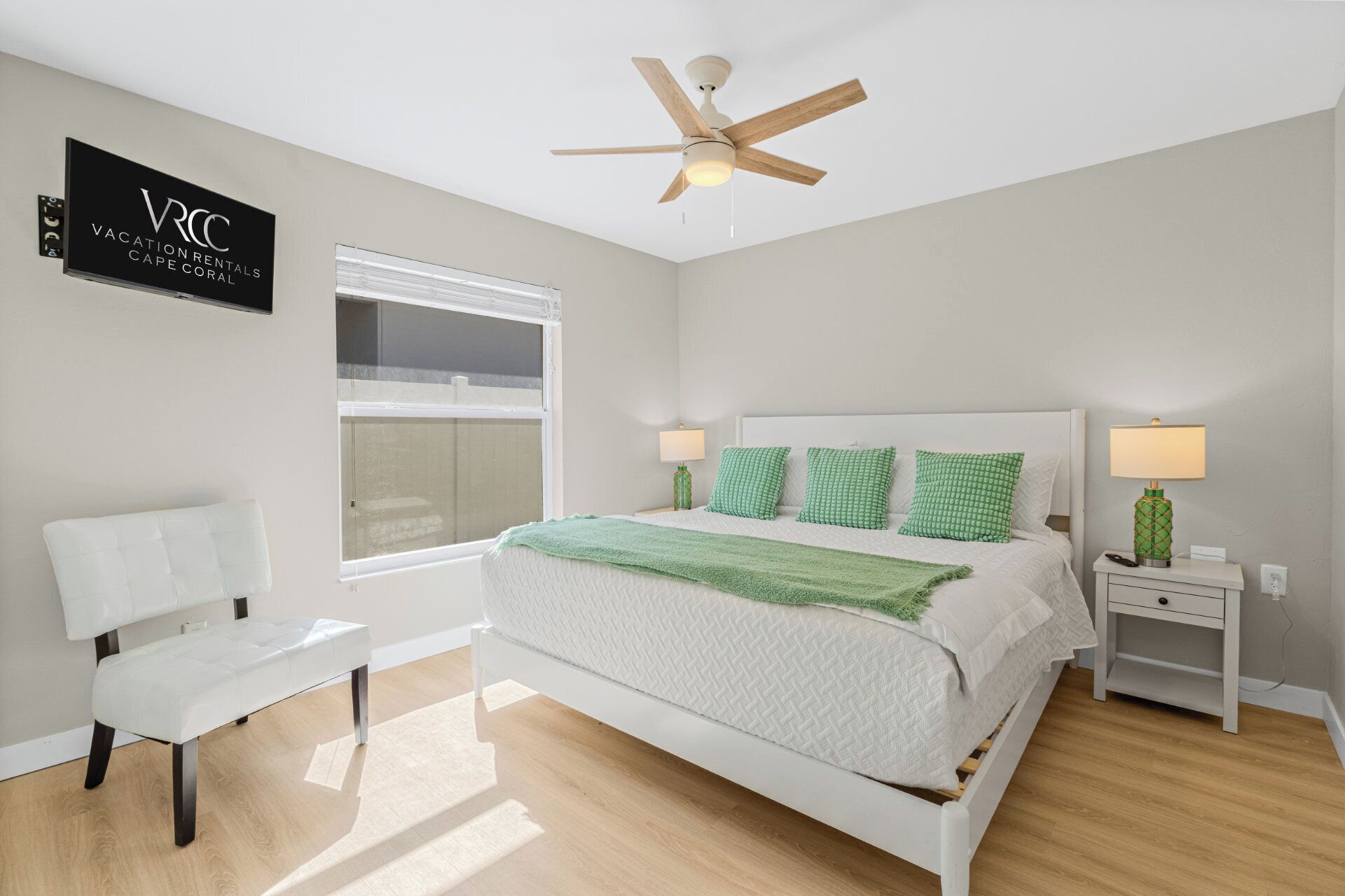 A modern bedroom with a bed, two bedside tables, a bench, a ceiling fan, and a window.