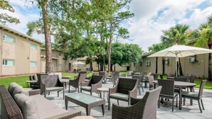 Un espace extérieur aménagé en terrasse, avec des meubles en osier, notamment des canapés et des tables, entouré d’arbres et d’un bâtiment.