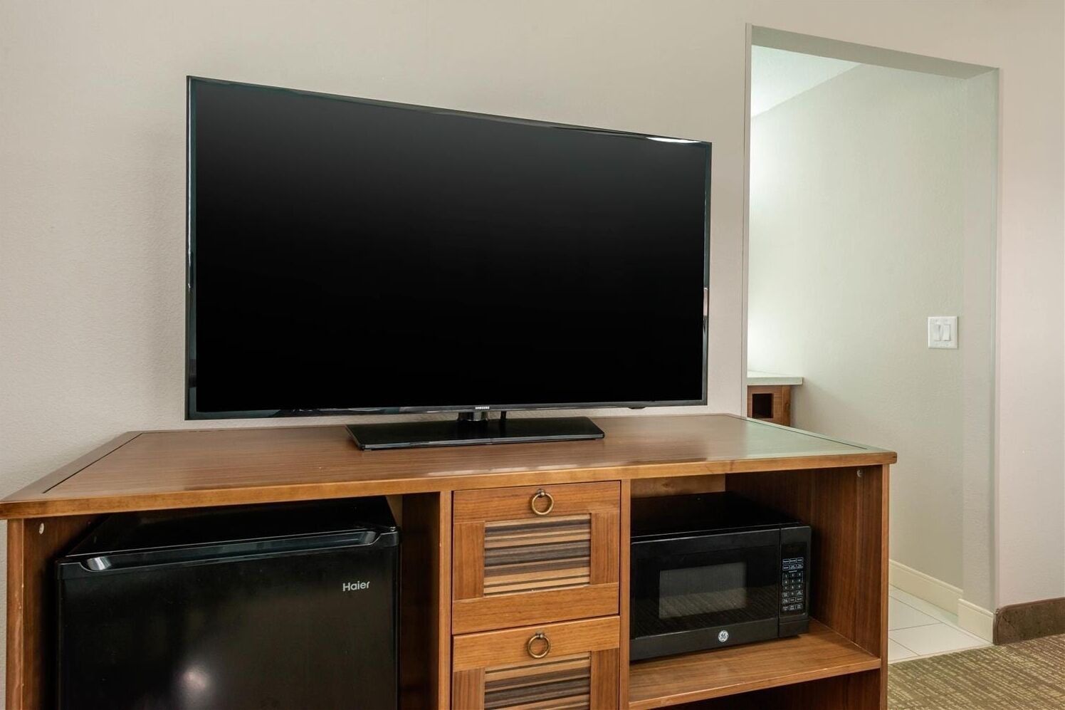 Un mueble de entretenimiento de madera con un televisor de pantalla plana, un mini refrigerador Haier y un microondas.