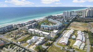 Vista aérea de uma área de resort costeira com vários edifícios, incluindo hotéis e complexos residenciais, perto de uma praia.