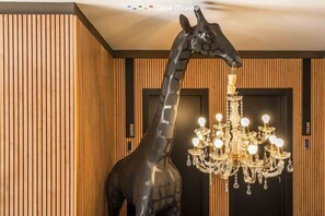 Una estatua de jirafa al lado de un candelabro en una habitación con paneles de madera y una puerta con la leyenda 'GARDEN'.