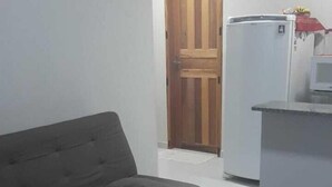 A living room with a sofa and a small table, a wooden door, and a kitchen area with a refrigerator. - Charming 1-bedroom apartment in Armação dos Búzios perfect for relaxing (Armação dos Búzios)