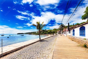 A coastal walkway with cobblestone pavement, wooden boardwalk, and buildings with blue shutters. - Charming 1-bedroom apartment in Armação dos Búzios perfect for relaxing (Armação dos Búzios)