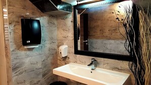A bathroom with a marble wall, a white sink, a mirror, and a soap dispenser. - Apart Hotel Solaris: Deluxe Apartment 4: 30 m2 (Skopje)