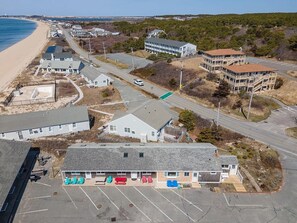 Eine Vogelperspektive zeigt eine Küstenlandschaft mit einer Reihe von Strandhäusern, einem Parkplatz und einer Straße, die zum Strand führt.