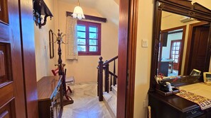 Eine Holztreppe mit Handlauf, ein Fenster mit Vorhängen und ein Spiegel, der ein Zimmer mit einem Bett und einer Kommode reflektiert.