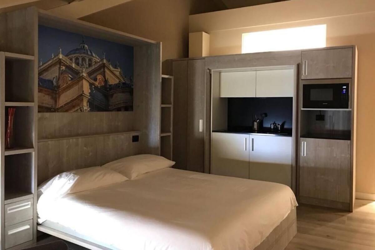 A bedroom with a bed, a wardrobe, a built-in microwave, and a painting on the wall.