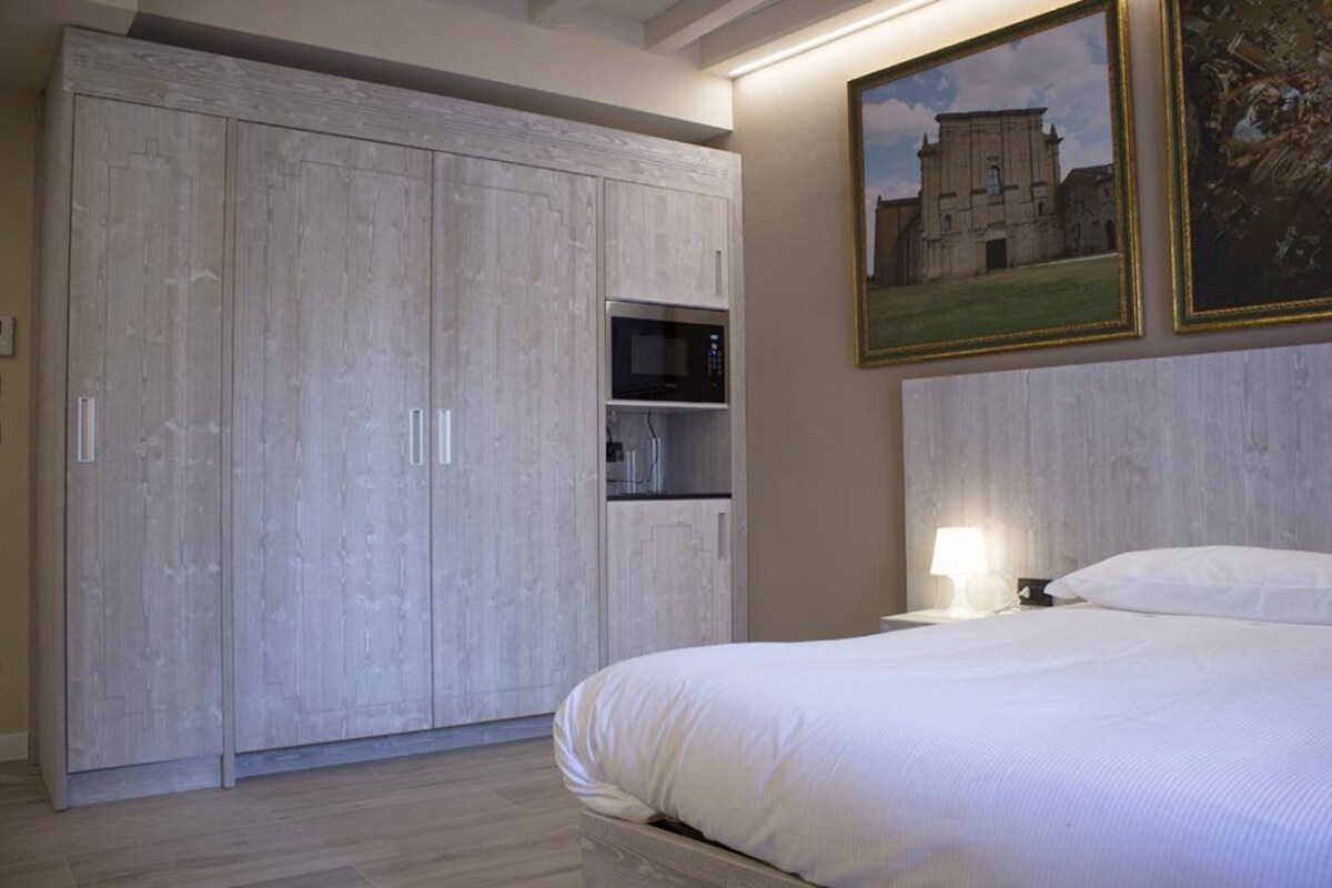 Un dormitorio con un armario grande, una cama, una mesita de noche con una lámpara y un cuadro enmarcado en la pared.