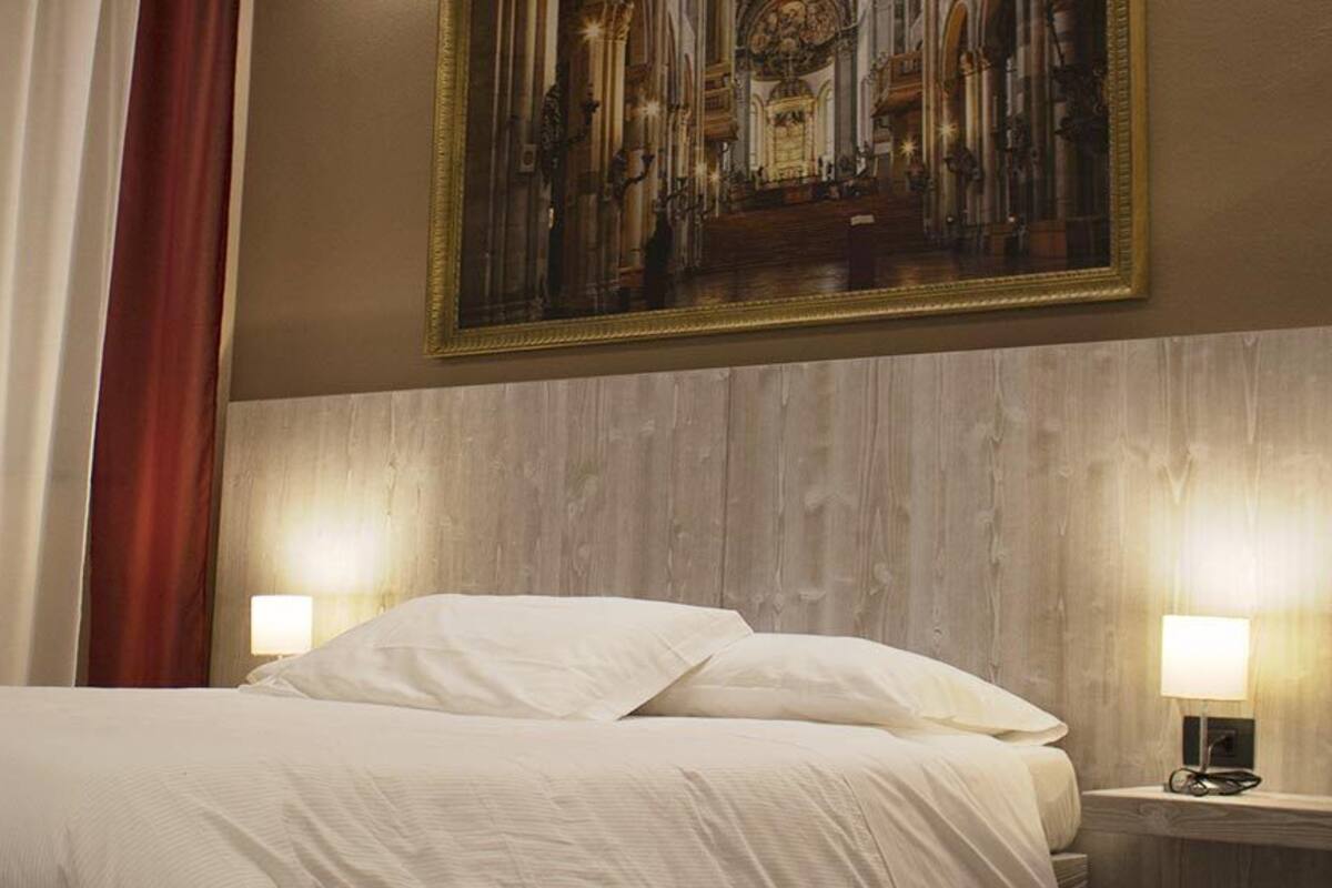A hotel room with a bed, curtains, a painting, and two bedside lamps.