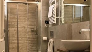 A modern bathroom with a glass shower enclosure, two sinks, a toilet, and a vanity with a mirror and towel rack. - Palazzo Domanto Parma Apartments (Parma)