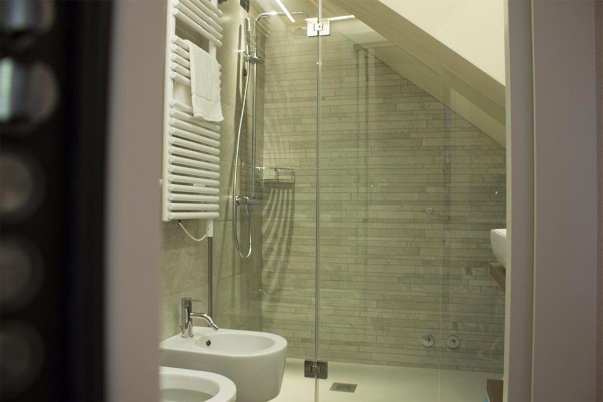 A modern bathroom with a glass shower enclosure, a white sink, and a tiled wall.