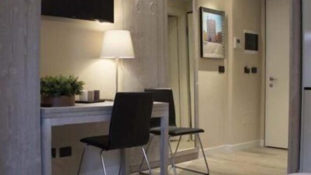 A hotel room with a bed, a desk with a chair, a lamp, a potted plant, and a framed picture on the wall. - Palazzo Domanto Parma Apartments (Parma)
