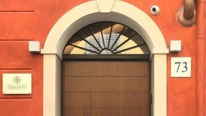 A wooden door with a metal handle, flanked by a white and orange wall, and a number '73' sign above it. - Palazzo Domanto Parma Apartments (Parma)