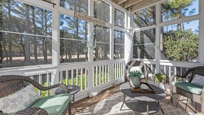Eine überdachte Veranda mit Korbmöbeln, einem Tisch und einem Schild mit der Aufschrift 'Life is Better on the Porch'.