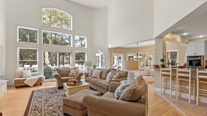 Ein geräumiges Wohnzimmer mit großem Fenster, einer Sofagarnitur und einer Küchenzeile mit Barhocker.
