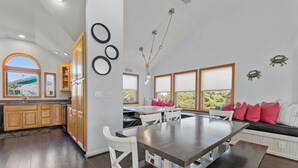 Una cucina moderna con mobili in legno, un'area pranzo con un tavolo grande e un angolo relax con vista sul verde.