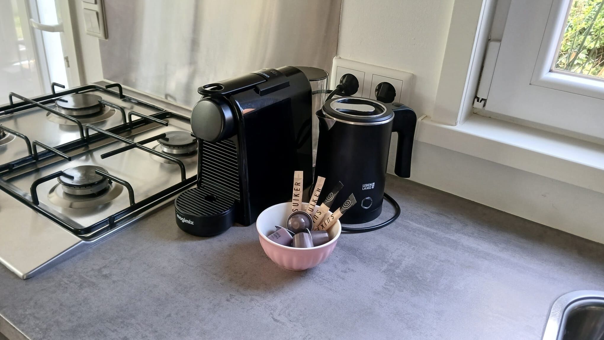 A kitchen with a gas stove, a coffee maker, and a bowl with utensils.