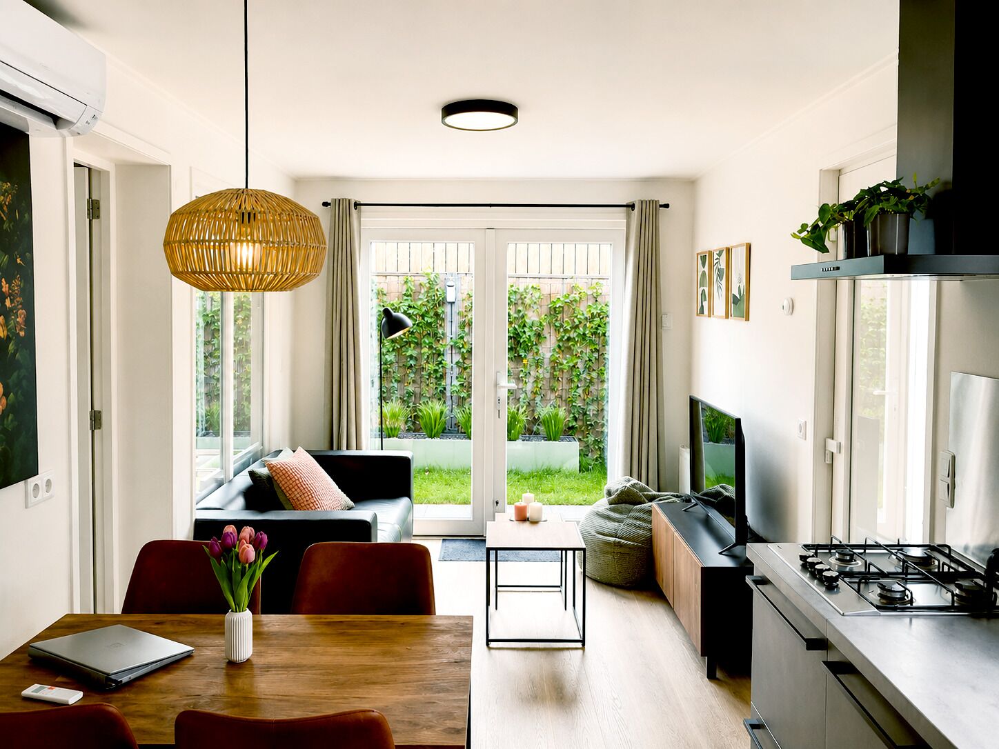 A modern kitchen with a gas stove, a dining area with a laptop, and a living room with a sofa and a TV.