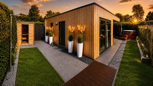 Un bâtiment moderne en bois, doté d’une porte en verre, entouré d’un jardin bien entretenu et agrémenté d’une terrasse en bois.