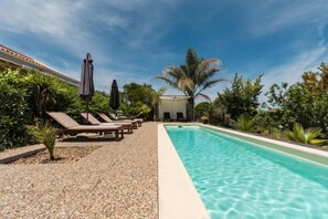 Una piscina con lettini e ombrelloni, circondata dal verde.