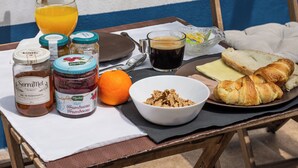 Une table de petit-déjeuner avec un verre de jus d’orange, une tasse de café, des pots de confiture, un bol de céréales, du pain et des croissants.