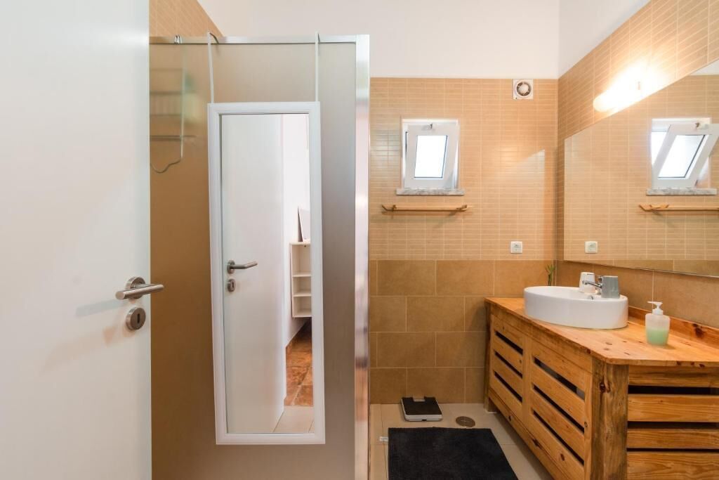 A bathroom with a white door, a wooden vanity, a mirror, and a small window.