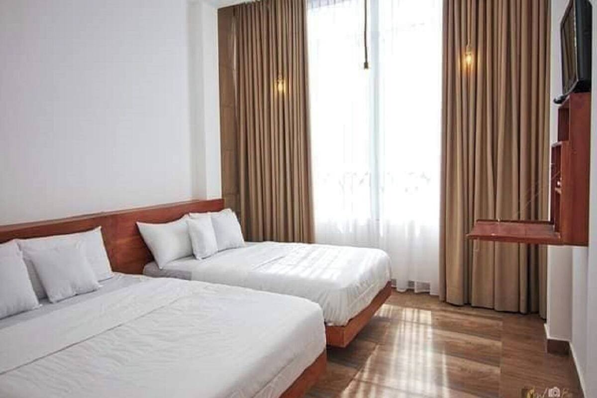 A hotel room with two beds, wooden headboards, a flat-screen TV, and a large window with curtains.