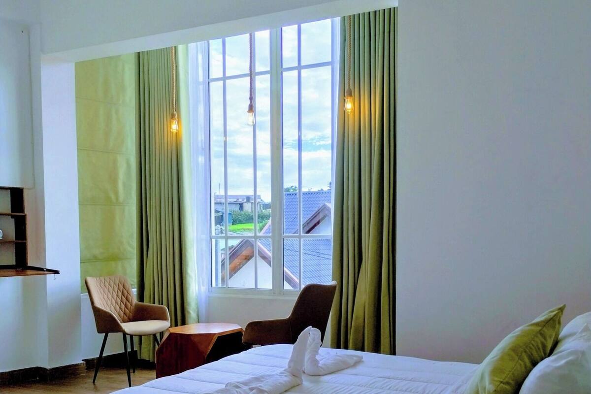 A hotel room with a large bed, a desk, two chairs, and a window with curtains.