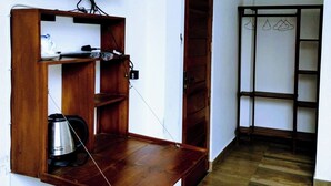 A room with a wooden desk, a television mounted on the wall, a door, and a shelving unit with a hanging clothes rack. - Pensive Villa - Nuwara Eliya (Nuwara Eliya)