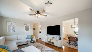 A modern living room with a sofa, coffee table, and TV. There is a dining area with a table and chairs. - 4BR LU Getaway! 4 Min to LU • Hot Tub • Game Room (Lynchburg)