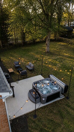 Un patio trasero con jacuzzi, mobiliario exterior e iluminación con luces colgantes.