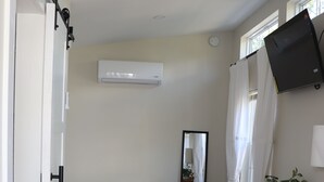 Une chambre à coucher de taille modeste, comprenant un lit, un bureau, un miroir et une plante en pot.