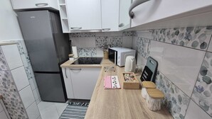 Una cocina compacta con armarios blancos, un refrigerador de acero inoxidable, un microondas y una pequeña encimera cubierta con un mantel a cuadros y recipientes de madera.