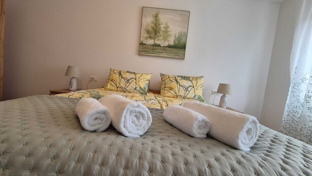 Un dormitorio con una cama grande, dos almohadas y dos toallas enrolladas.