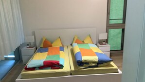 En dobbeltseng med farverigt sengetøj, et natbord og et vindue med udsigt.