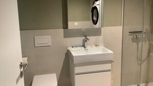 Et badeværelse med toilet, håndvask, spejl og bruser.