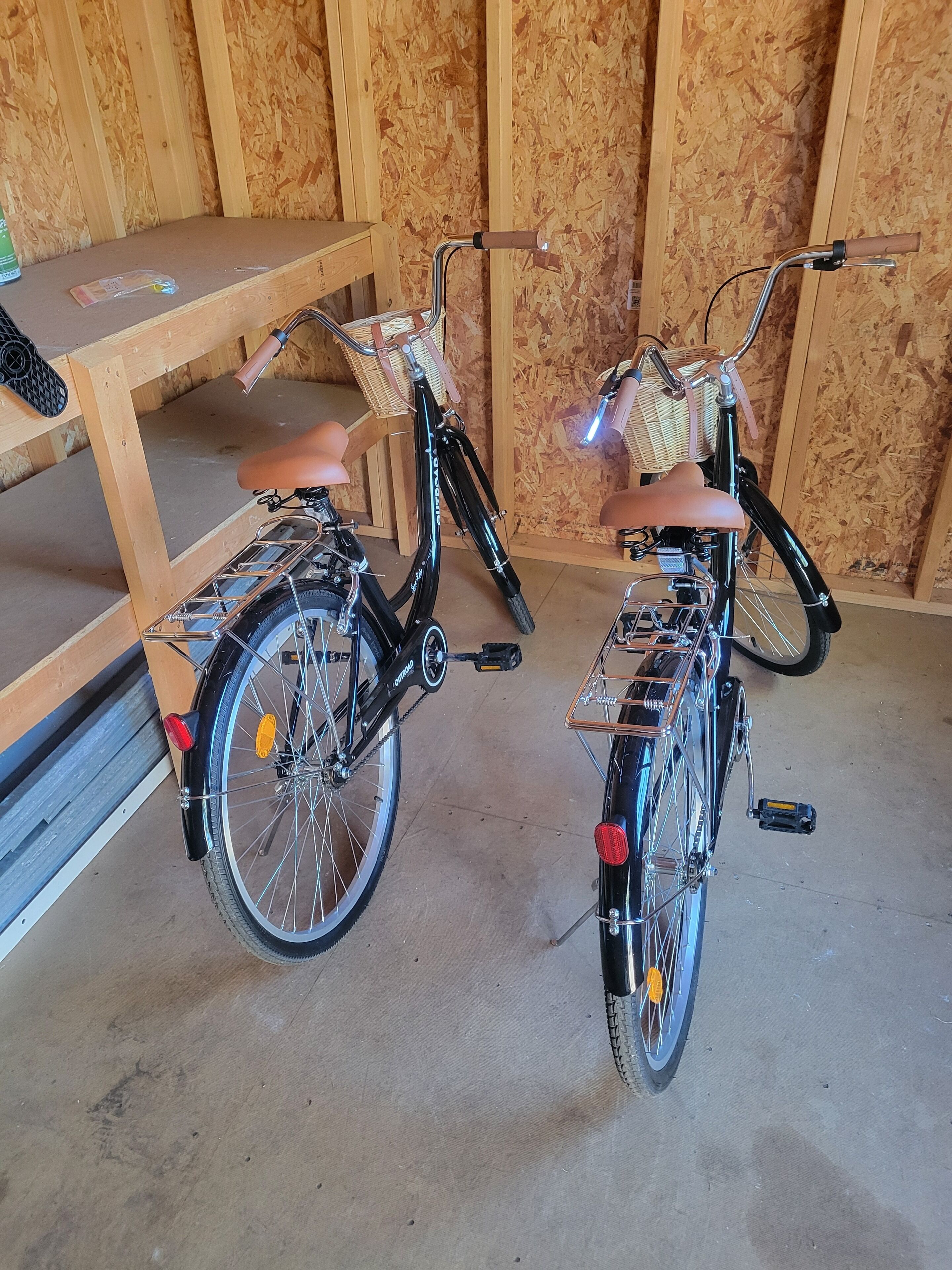 Deux vélos équipés de paniers et de béquilles sont garés à l’intérieur, appuyés contre un mur en bois.