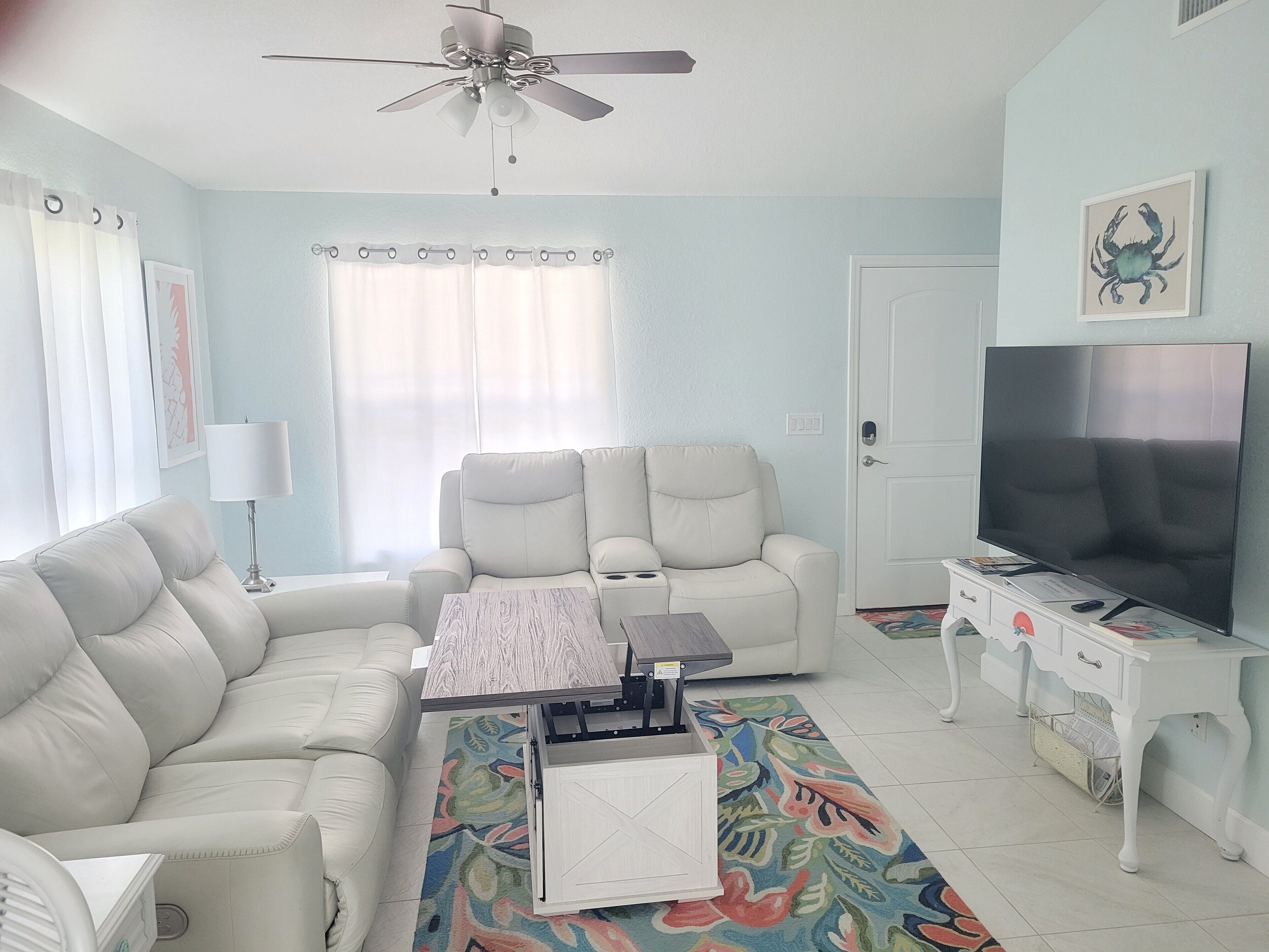 A living room with a sofa, two armchairs, a coffee table, a TV, and a ceiling fan.
