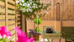 Een terras met een houten trellis, een tafeltje voor twee met stoelen, en een bloemarrangement dat hangt.